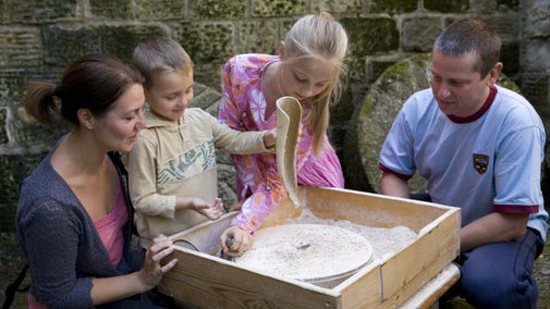 A family having a go at an activity to grind flour at Stainsby Mill, Derbyshire